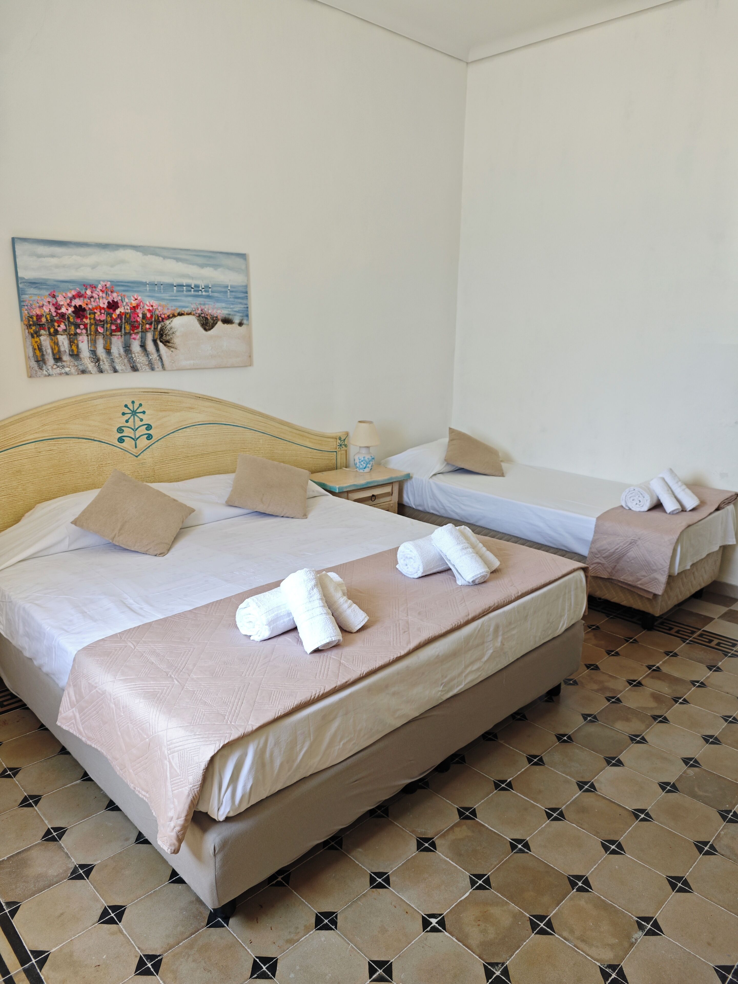 Quarto de hotel com duas camas, um quadro na parede e chão de azulejos.