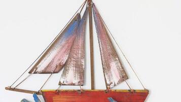 A model sailboat with a red hull and blue and red sails.