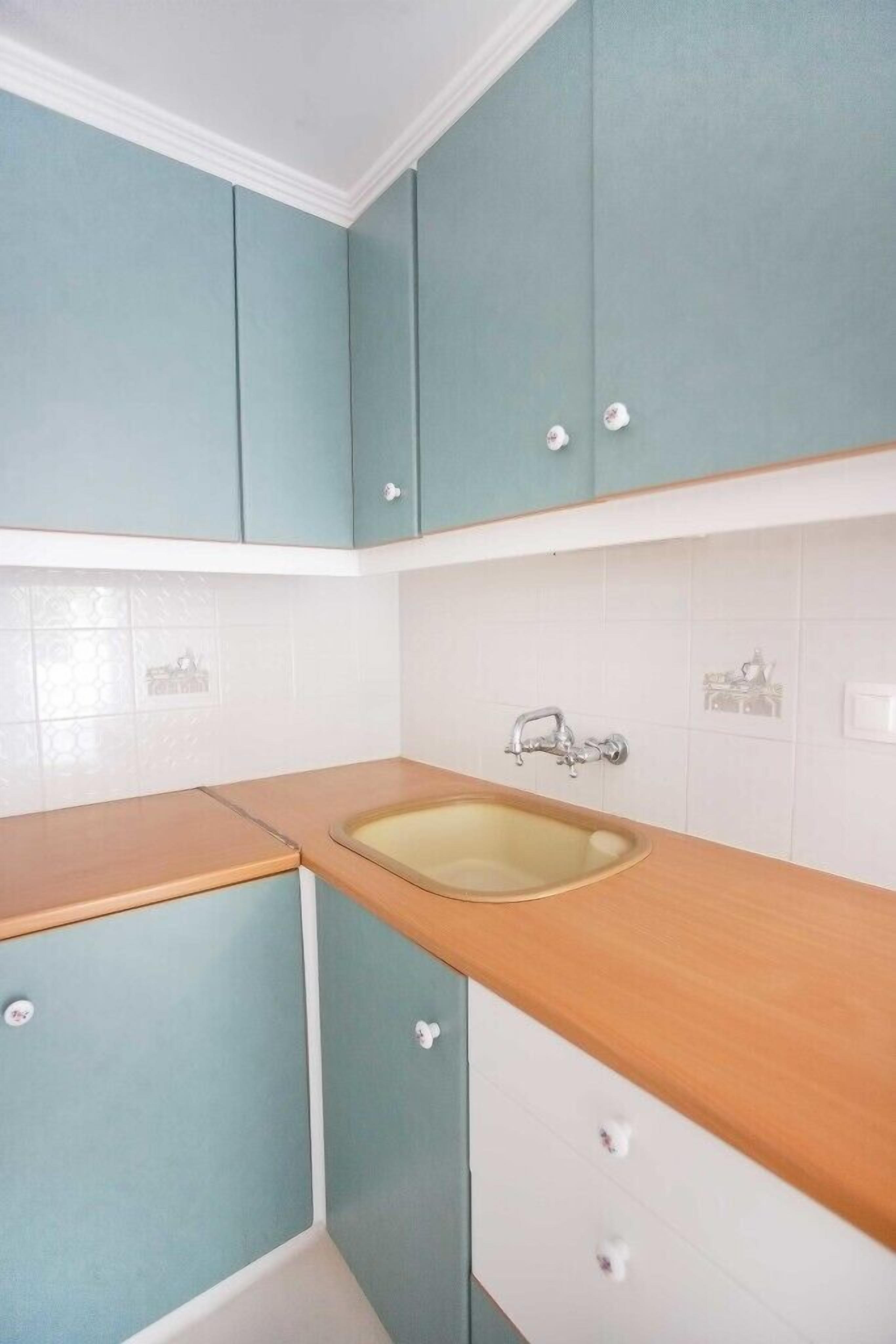 A kitchen with teal cabinets, a wooden countertop, and a sink.
