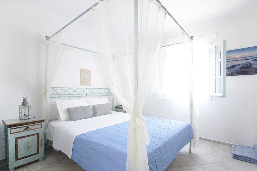 A bedroom with a four-poster bed, a nightstand, a lamp, and a painting on the wall.
