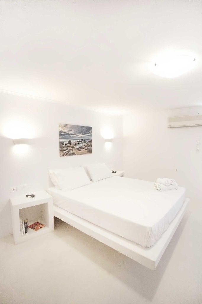 A minimalist white bedroom with a bed, bedside tables, and a wall-mounted air conditioner.
