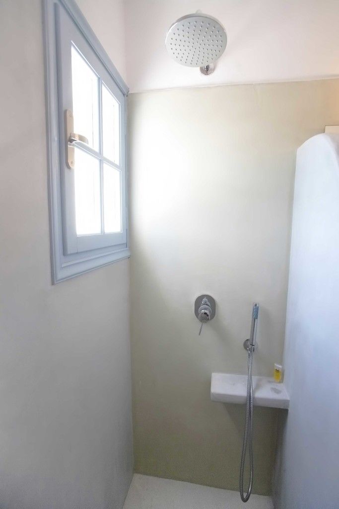 A small bathroom with a shower, a window, and a sink.