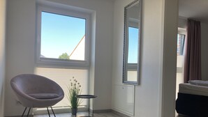 A modern room with a large window, a chair, a small table, and a mirror. - "bijoux - Juwel" im Haus Meeresjuwel! (Dahme)