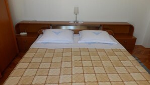A neatly made bed with a checkered bedspread, two pillows with a blue design, a bedside table with a lamp, and a wall-mounted light fixture.