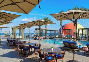 Uma área à beira da piscina com espreguiçadeiras e guarda-sóis, piscina e vista para o oceano.