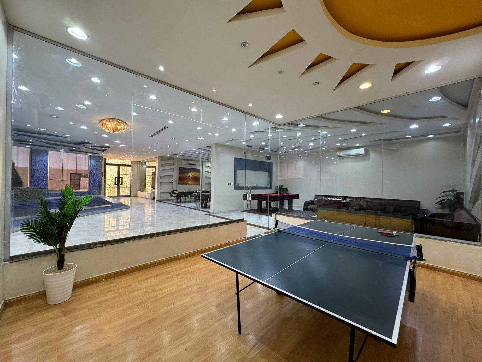 A spacious room with a ping pong table, a billiards table, and a seating area with a sofa and chairs.