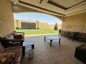 A spacious patio with a wooden floor, a sofa set, a small table, and a trash bin. - VIP resort chalet 19 (Riyadh)