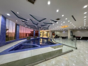 A spacious indoor swimming pool with a glass barrier, surrounded by a modern lobby with a high ceiling and recessed lighting. - VIP resort chalet 19 (Riyadh)
