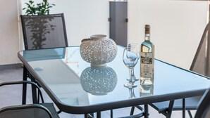 A glass table with a bottle of wine and a glass on it, a decorative bowl, and a chair. - Enjoy Summer from a lux flat steps to Sandy Beach (Maleme)