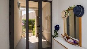 A modern interior with a sliding glass door leading to a patio, a white console table with decorative items, and a mirror with hats hanging on the wall. - Apartment Oaza (Supetar)