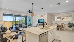 Una cocina amplia con una isla central, una zona de comedor con mesa y sillas, un sofá y una televisión.