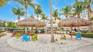 Un patio de resort con palmeras, sombrillas de paja y mobiliario exterior.