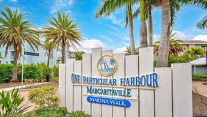 Señal para The Particular Harbour Maricavilla Marina Walk con un logotipo de un velero y palmeras.
