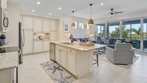 Una cocina moderna con armarios blancos, una isla central y un comedor con sofá y sillas.