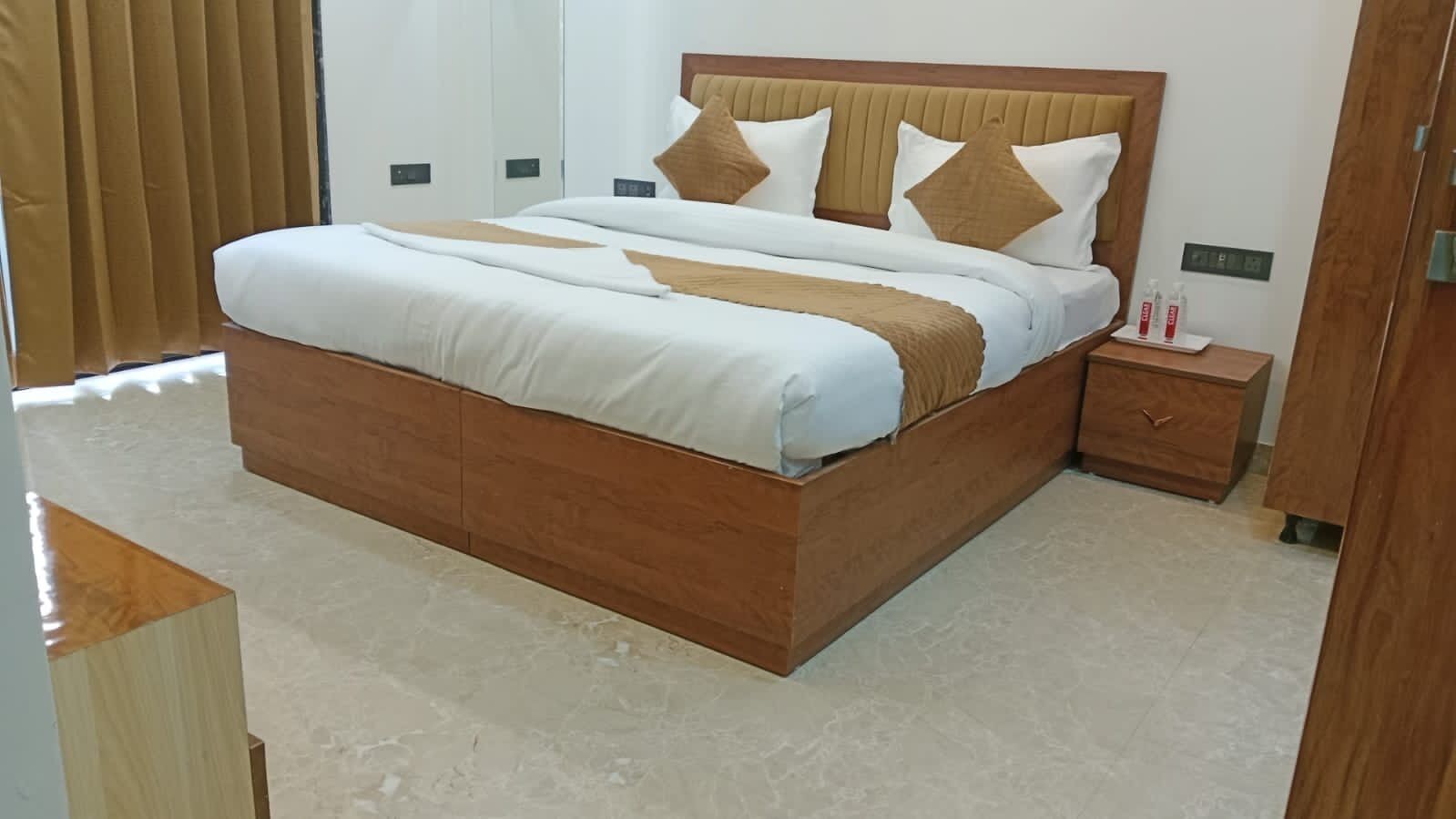 A neatly made bed with a wooden headboard, a bedside table with a bottle, and a wall-mounted clock.