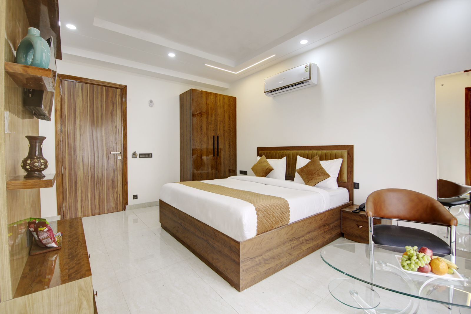 A modern bedroom with a wooden bed, a glass table with fruits, and a built-in wardrobe.