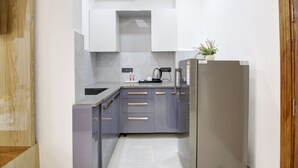 A modern kitchen with grey cabinets, a stainless steel refrigerator, and a small potted plant on the counter. - 360 Degree Hotel Medicity (Gurugram)
