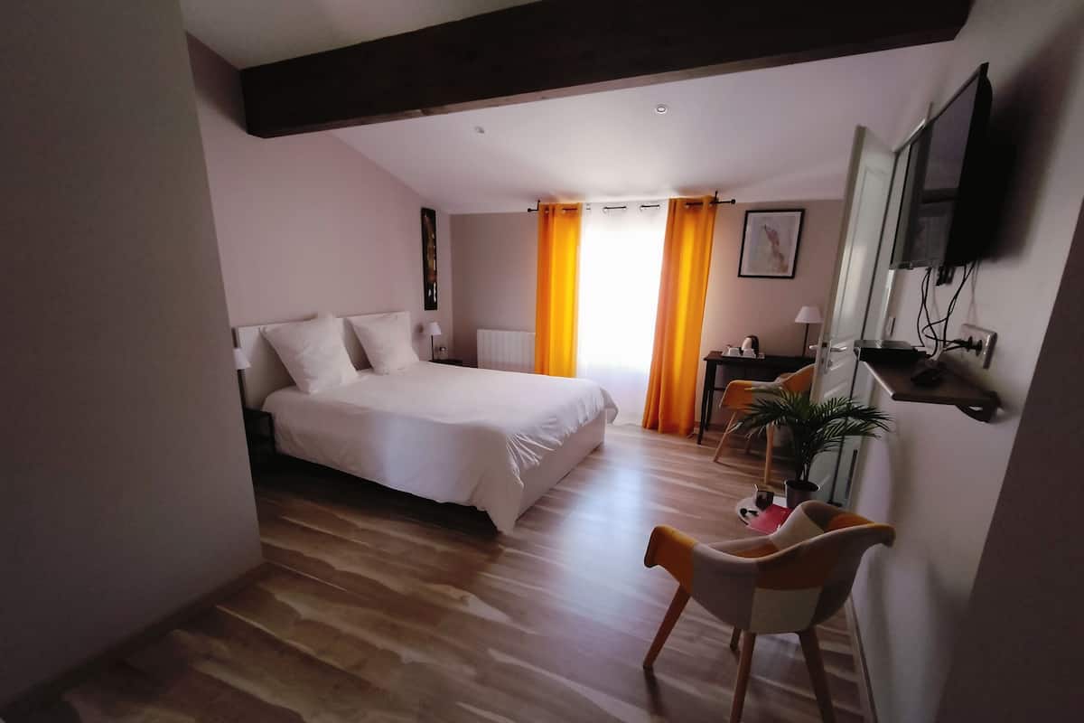 Ein Schlafzimmer mit einem großen Bett, einem Schreibtisch, einem Stuhl, einem Fernseher und einem Fenster mit Vorhängen.