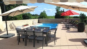 An outdoor pool area with a table and chairs, surrounded by umbrellas and lounge chairs. - Chambres d'hôtes "Au clocher" (Saint-Seurin-de-Cadourne)