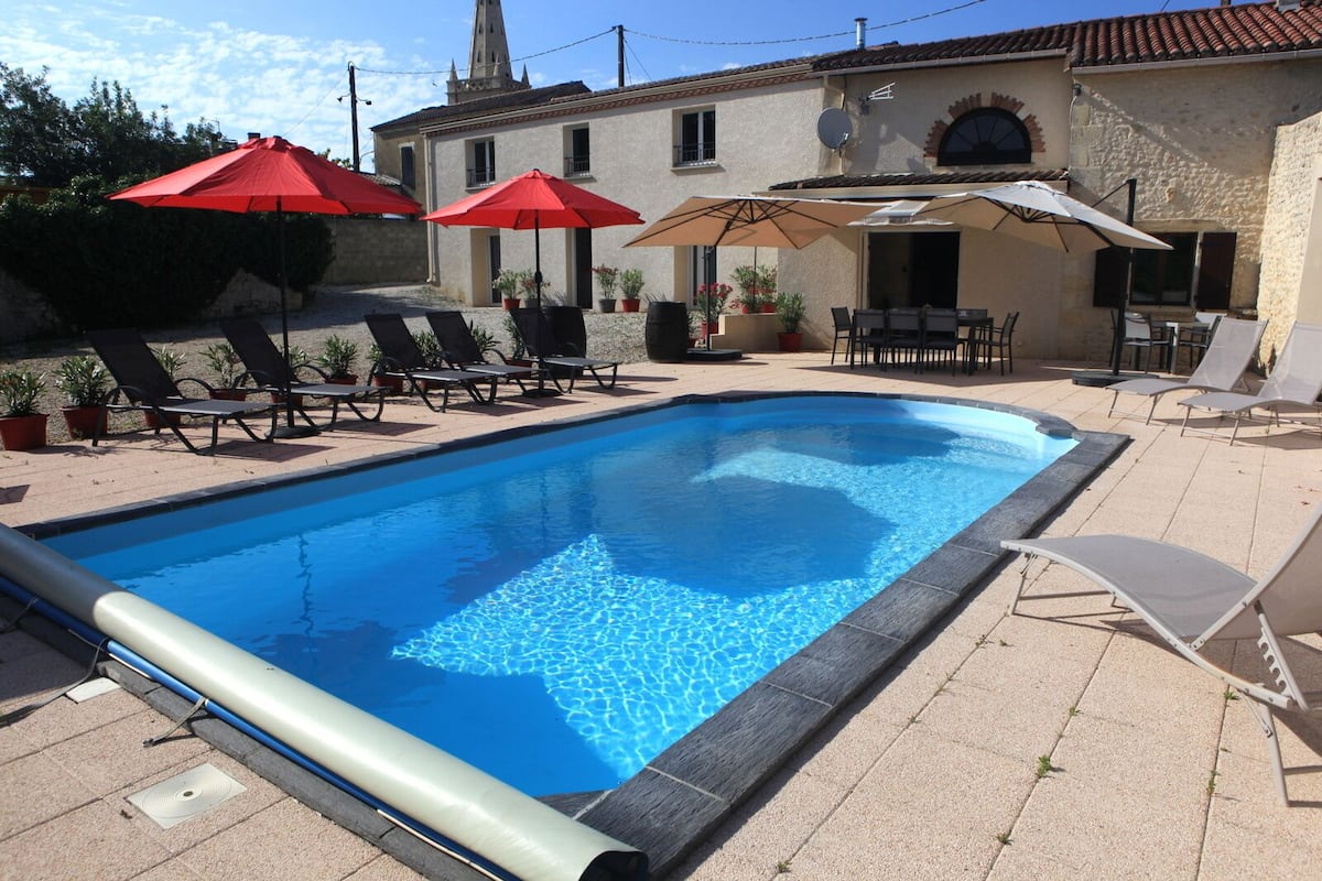 Ein Pool mit Liegestühlen und Sonnenschirmen, umgeben von einem Gebäude mit einem Ziegeldach und einer Steinauffassung.