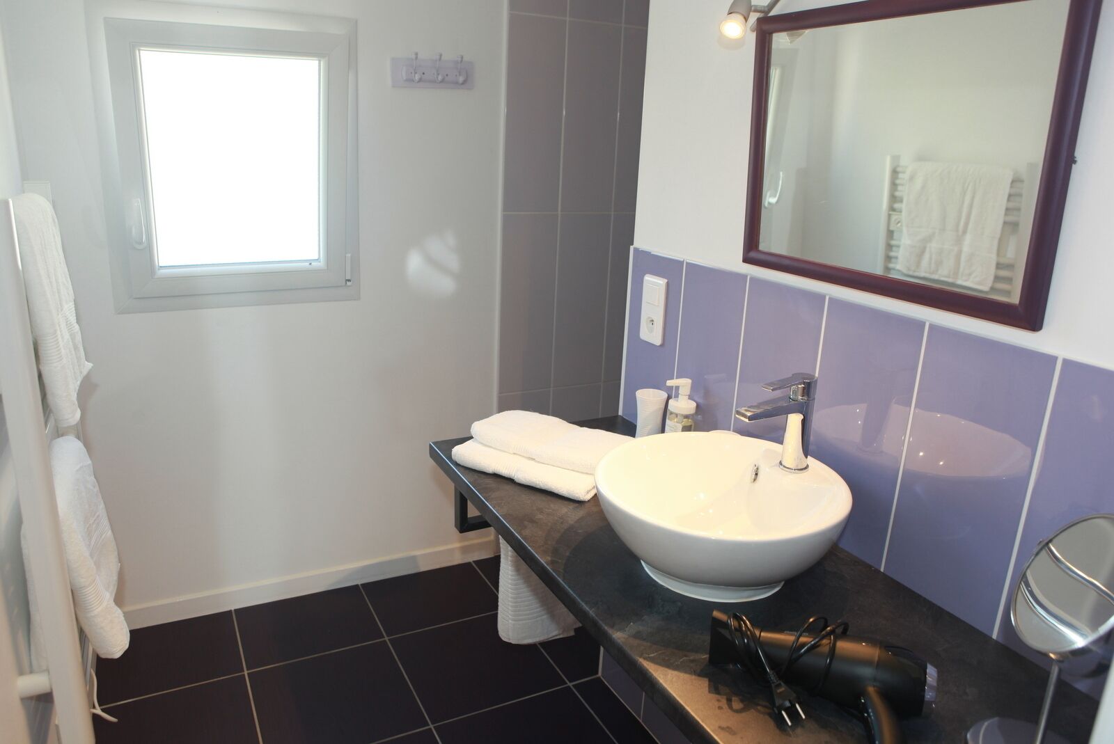 Een badkamer met een groot wastafel, een spiegel, een handdoekhouder en een raam.