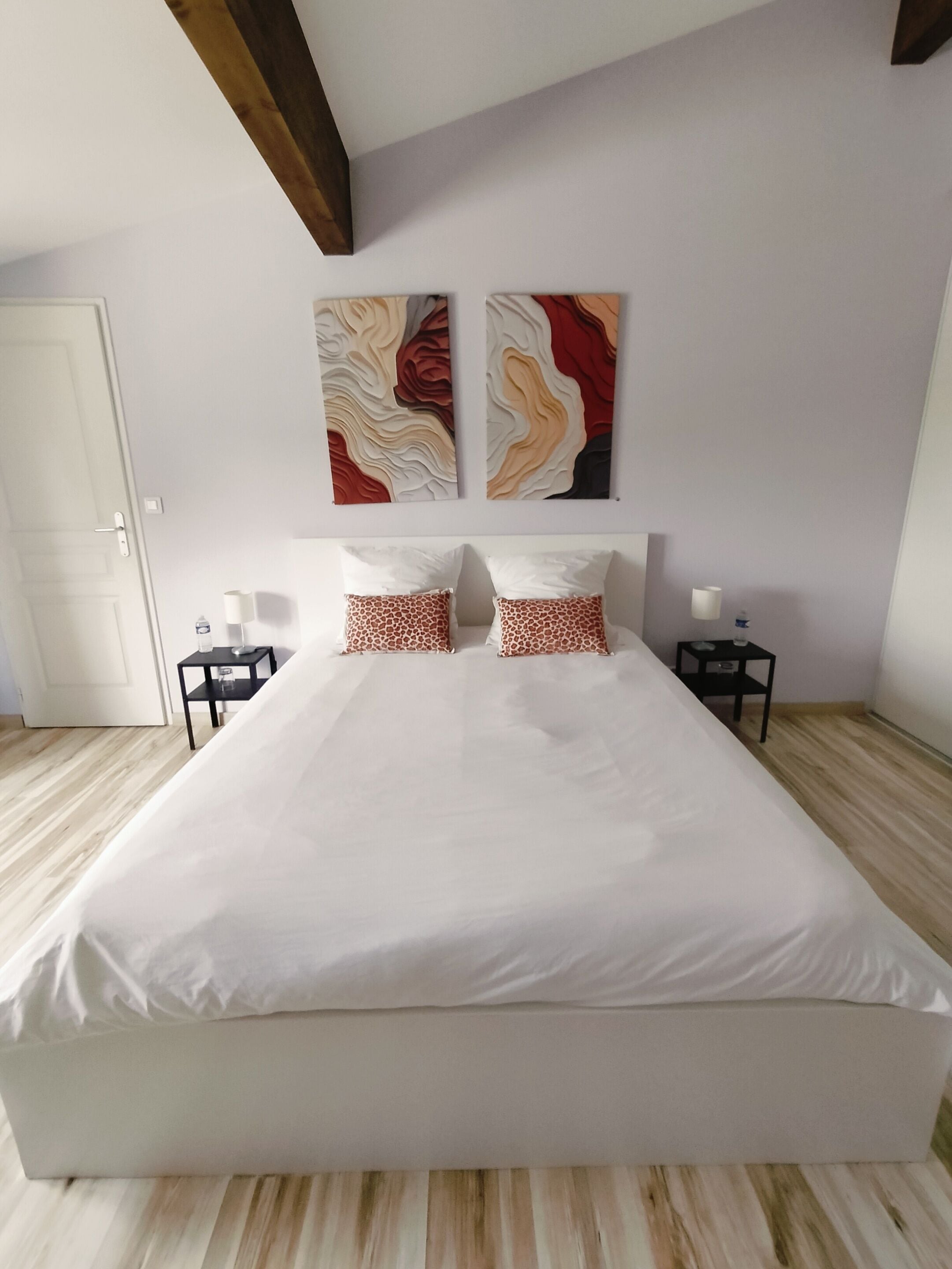 A bedroom with a large bed, two nightstands, a door, and abstract wall art.