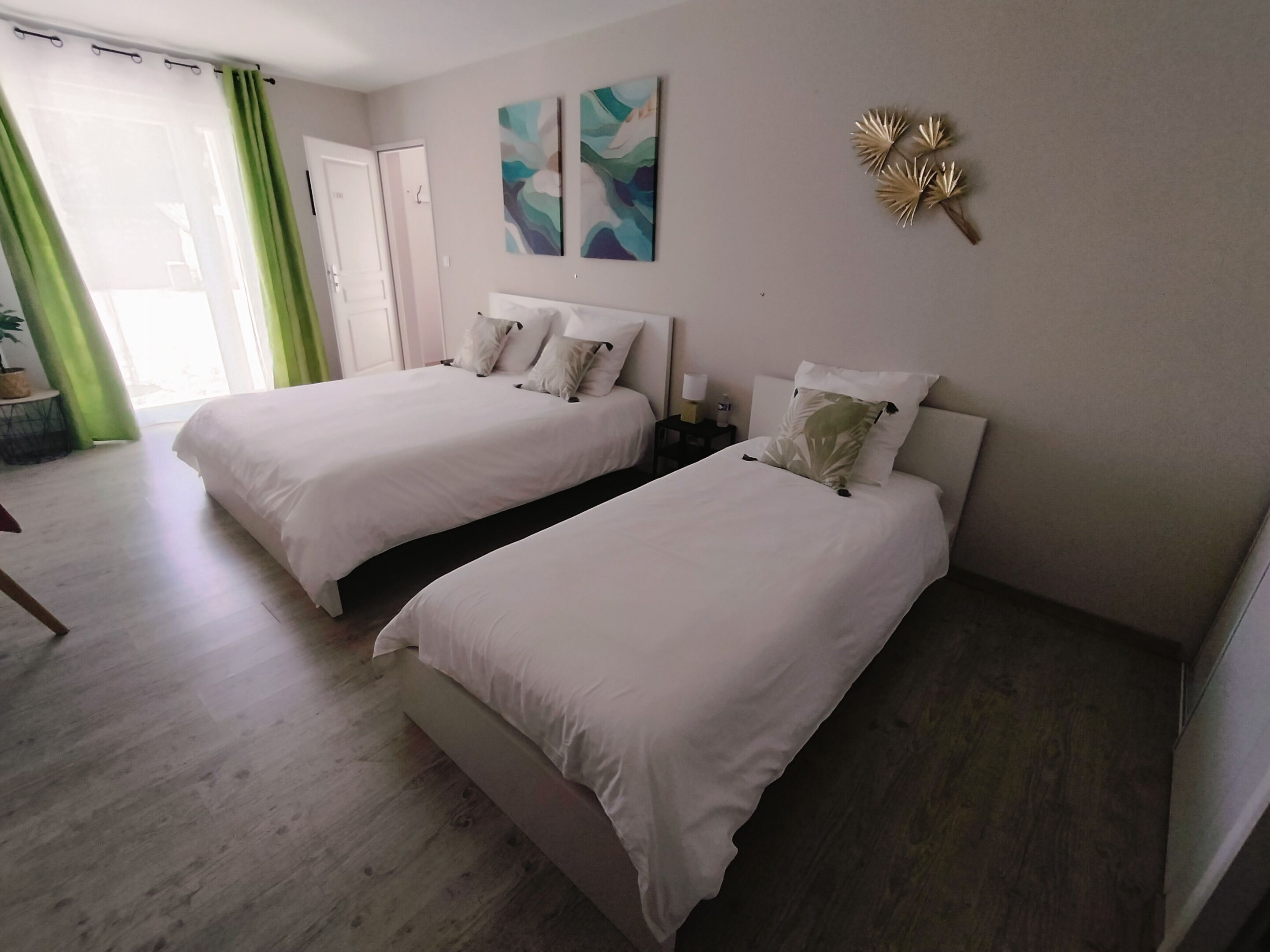 Habitación de hotel con dos camas, una ventana con cortinas verdes y un cuadro abstracto en la pared.