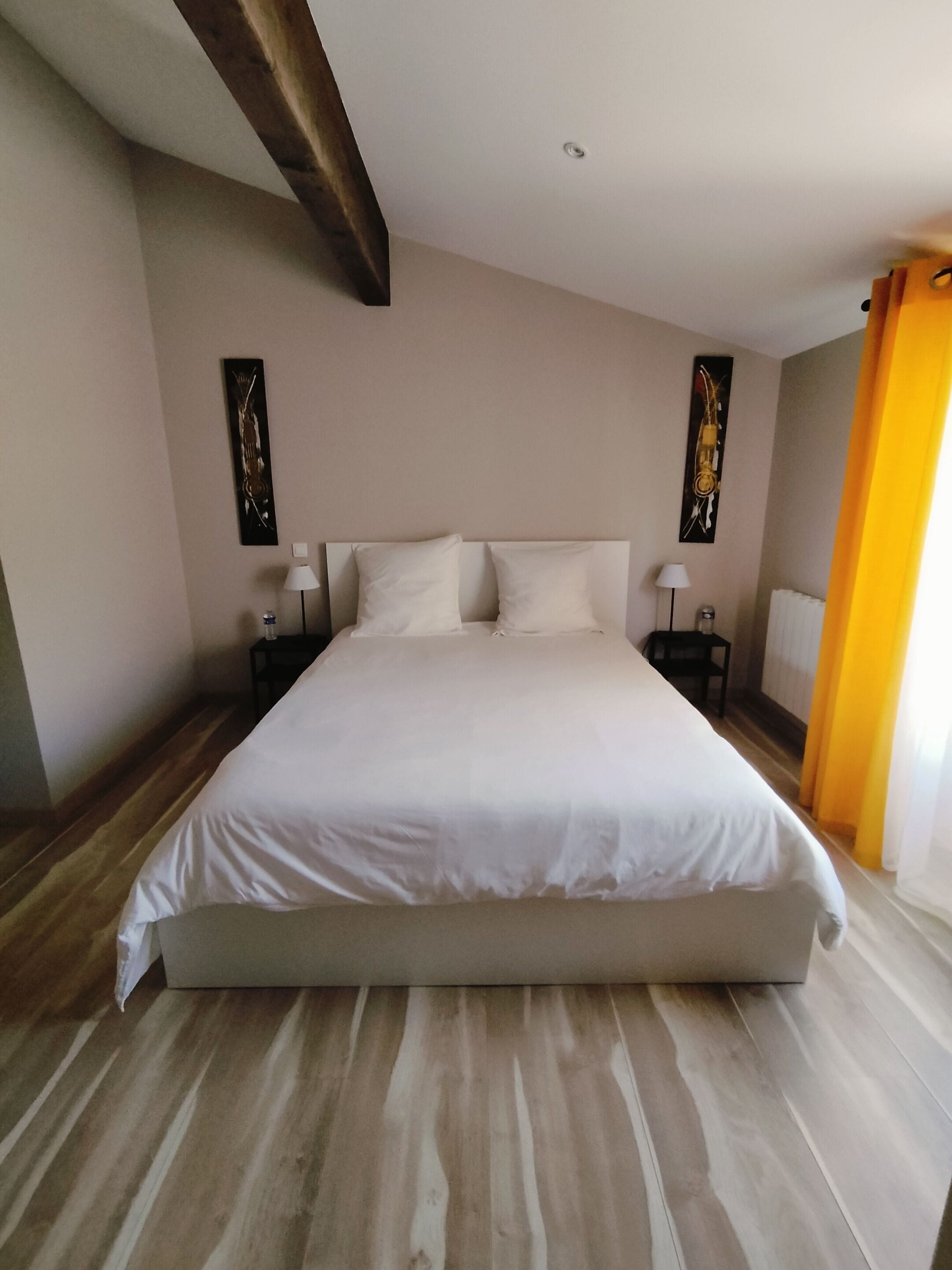 Un letto grande con lenzuola bianche, due comodini con lampade e opere d'arte alle pareti.