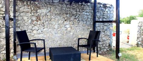 An outdoor patio with two black chairs and a black table, set against a stone wall.