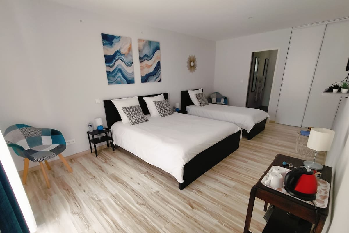 Ein Hotelzimmer mit zwei Betten, einem Sessel, einem kleinen Tisch mit Wasserkocher und Bildern an der Wand.
