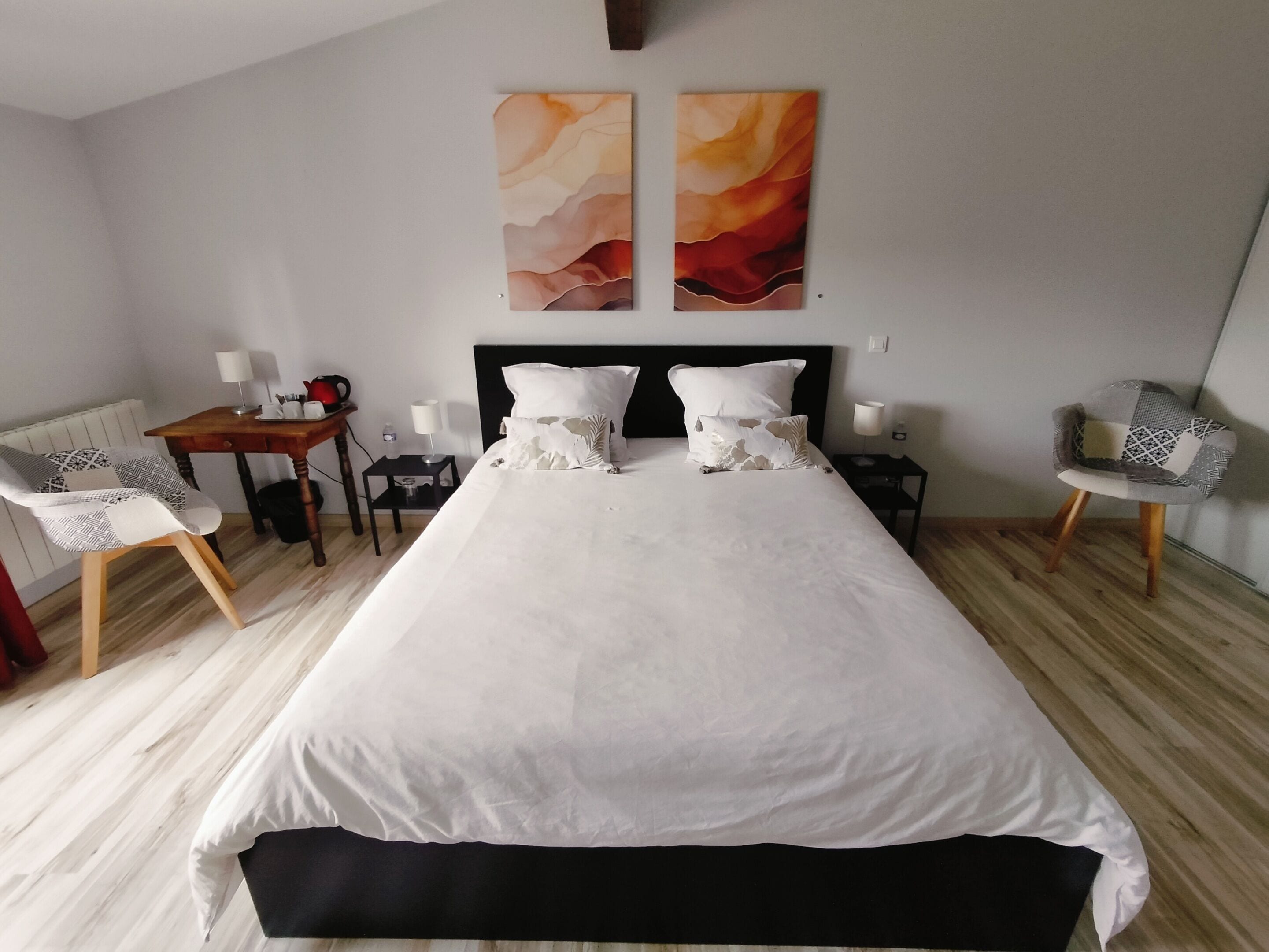 Ein Hotelzimmer mit einem großen Bett, zwei Nachttischen, einem Sessel und abstrakten Wandbildern.