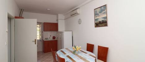 A dining area with a table set for four, a clock on the wall, and a view of the kitchen in the background.