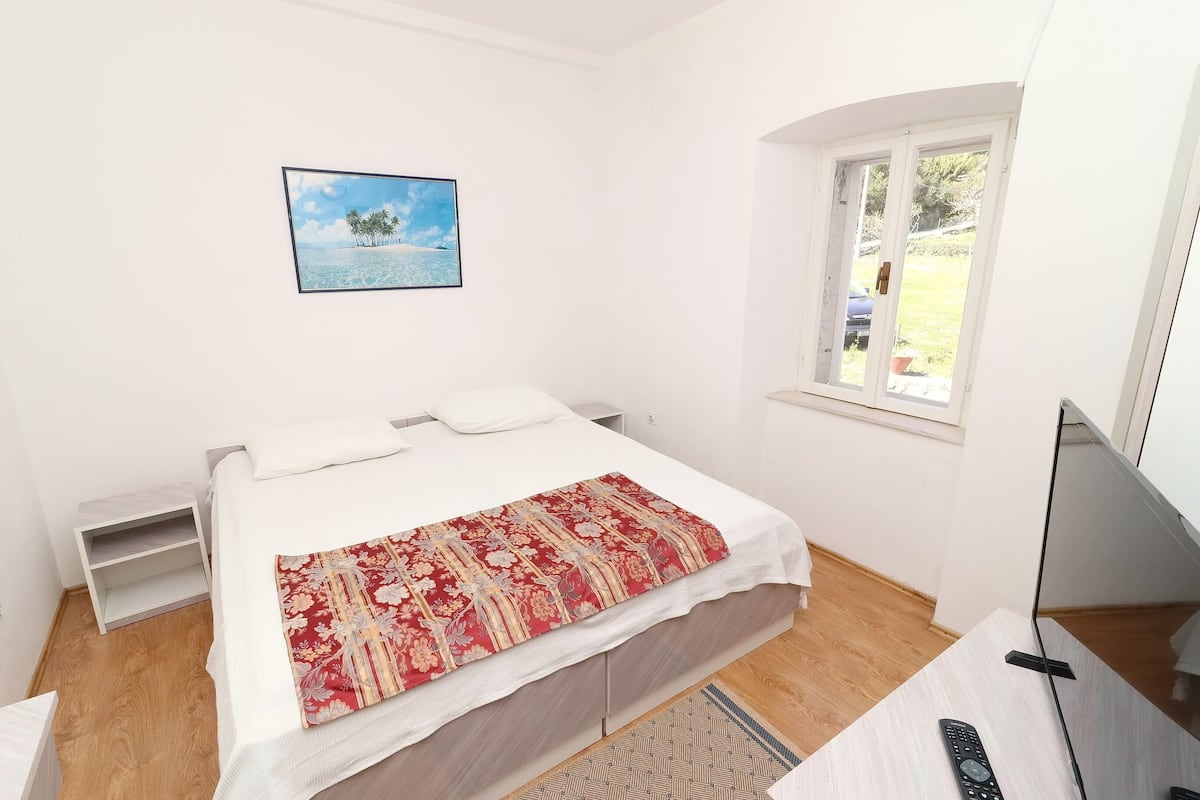 A bedroom with a bed, a window, a painting, and a TV.
