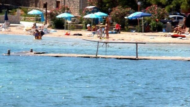 A beach with a swimming pool, umbrellas, and people relaxing.