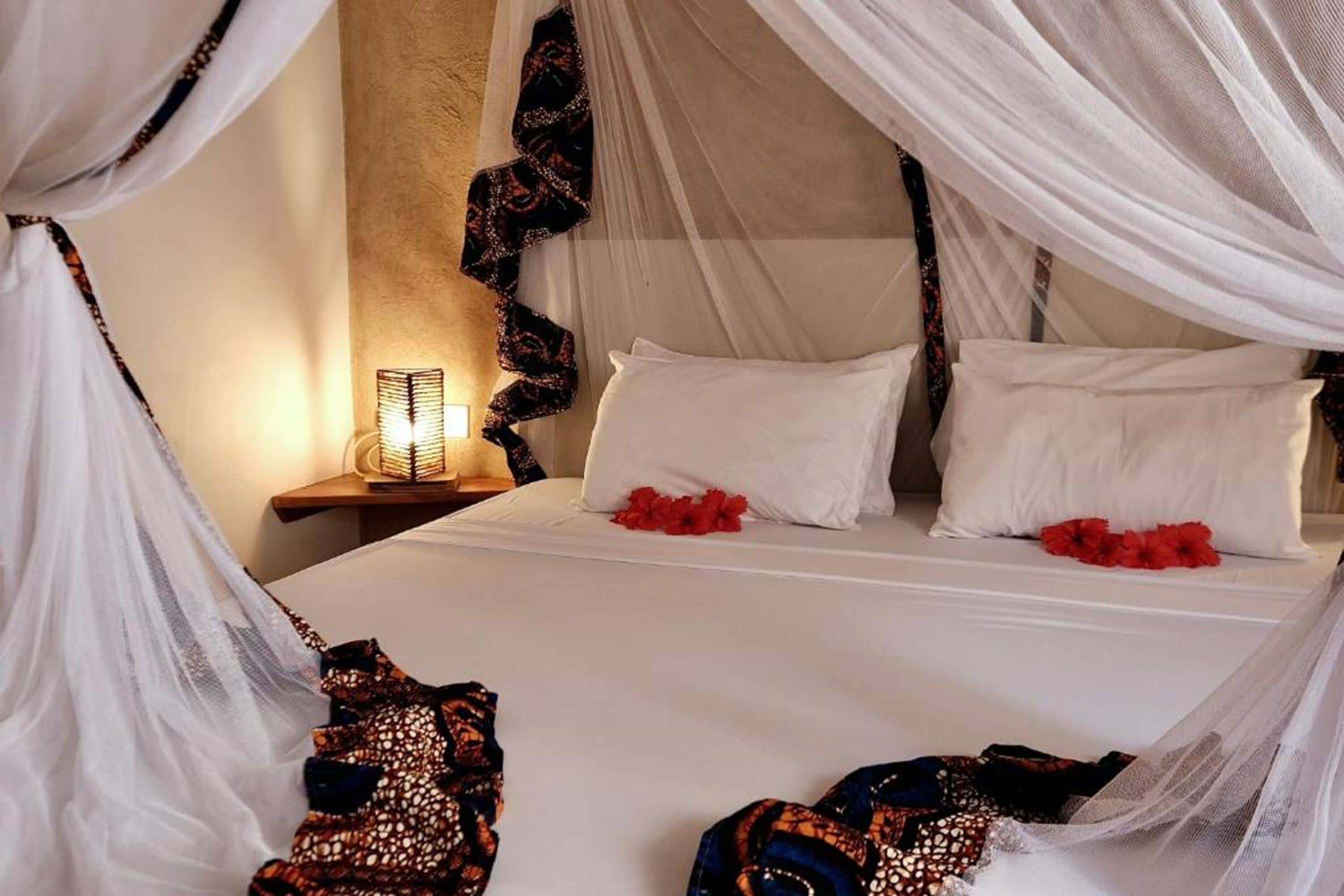 A bed with white linens, red flowers, and a canopy.