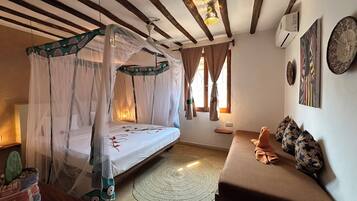Un dormitorio con cama con dosel, un sofá, una mesita y una planta decorativa.