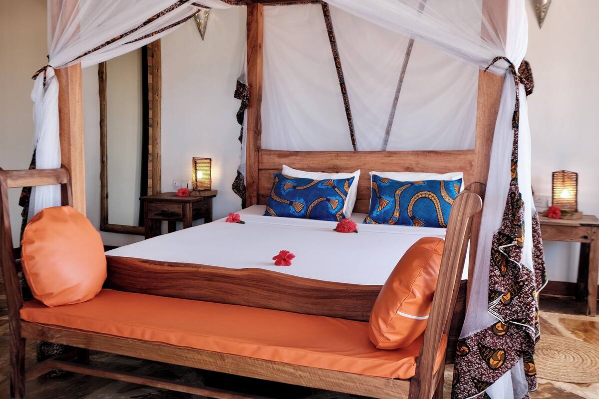 Una cama con dosel, cabecera de madera y cojines anaranjados.