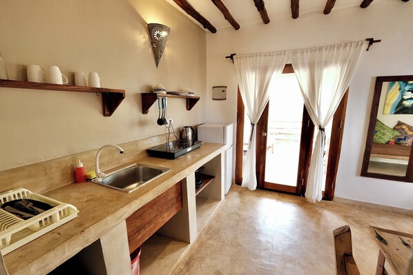 A kitchen with a wooden countertop, a sink, and a stove. There is a shelf with cups and a wall-mounted light. - LaPili Residence (Kiwengwa)