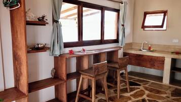 A rustic kitchen with wooden shelves, a stone floor, and a window with curtains.