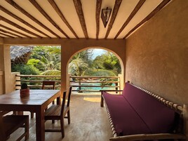 Una mesa de madera con un cojín y un banco en una habitación con vistas a una piscina y vegetación tropical.