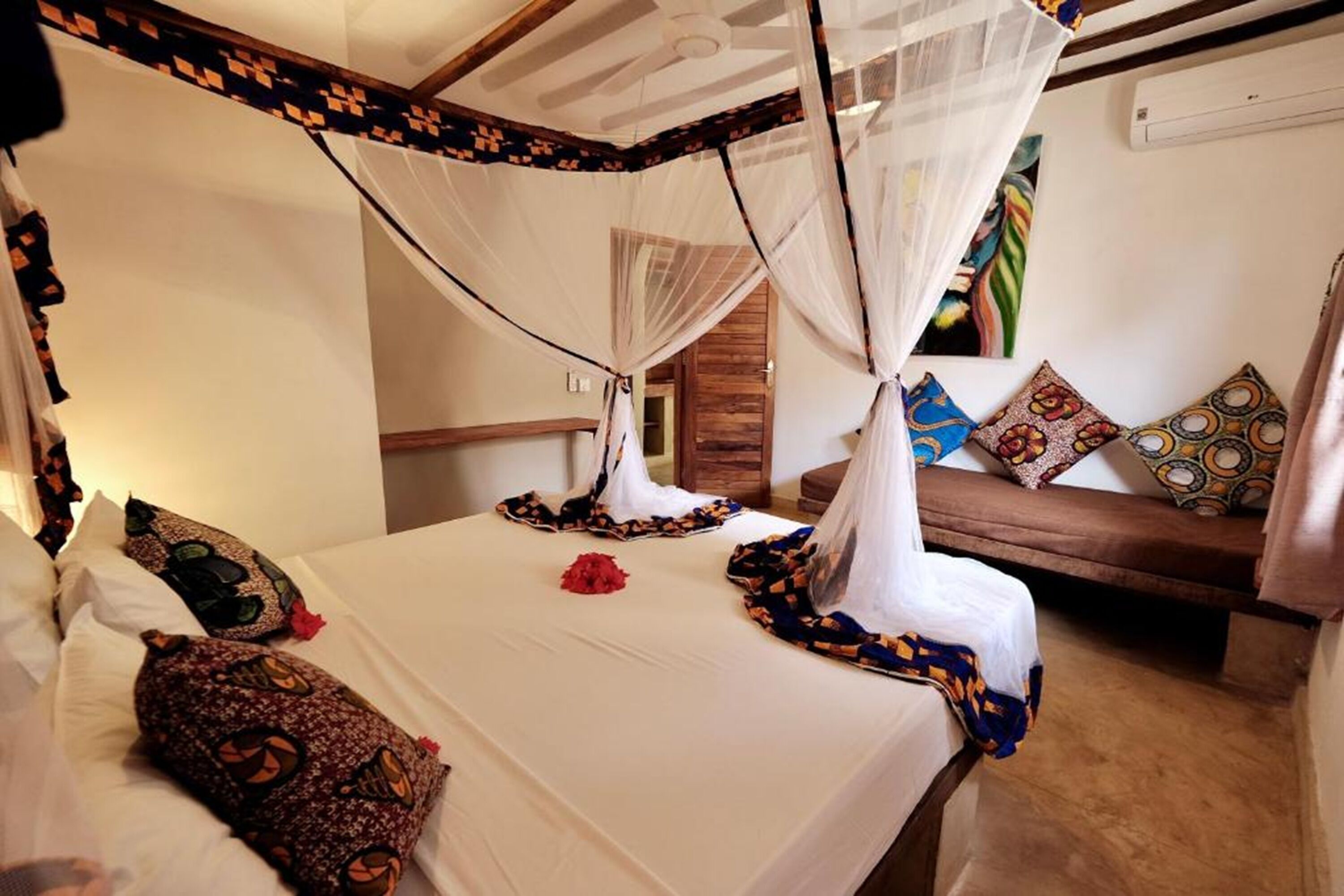 A room with a bed covered by a canopy, a sofa with patterned cushions, and a wall-mounted air conditioning unit.