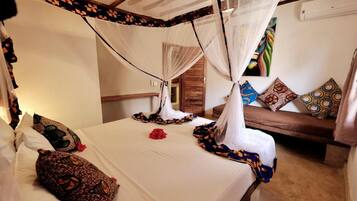 A room with a bed covered by a canopy, a sofa with patterned cushions, and a wall-mounted air conditioning unit.
