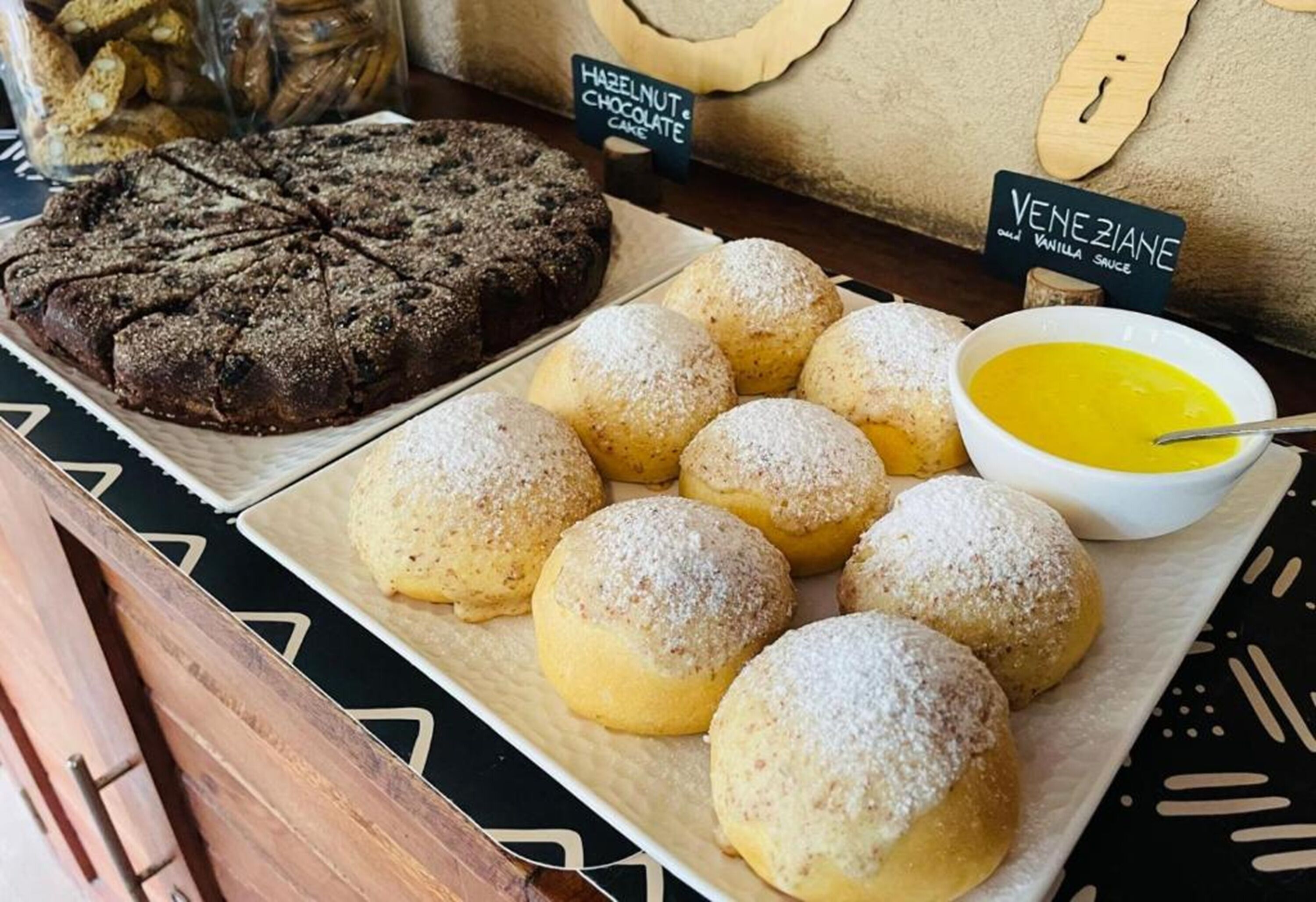 Una presentación de postres con pastel de chocolate, bollos azucarados y un tazón de salsa.