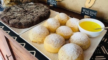 Una presentación de postres con pastel de chocolate, bollos azucarados y un tazón de salsa.