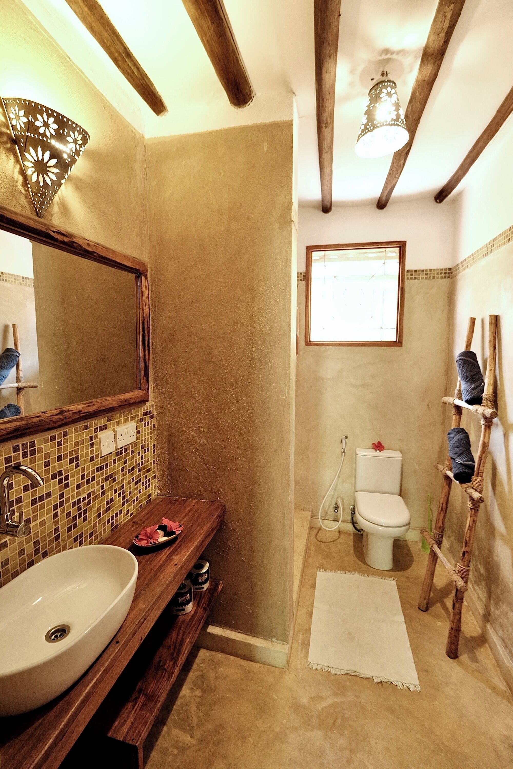 Ein Badezimmer mit einem Holzwaschtisch, einem großen Spiegel, einem weißen Waschbecken, einer Toilette und einem kleinen Fenster.