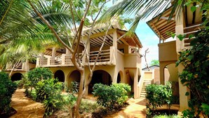 A courtyard with a covered walkway, palm trees, and a building with multiple arches and balconies. - LaPili Residence (Kiwengwa)