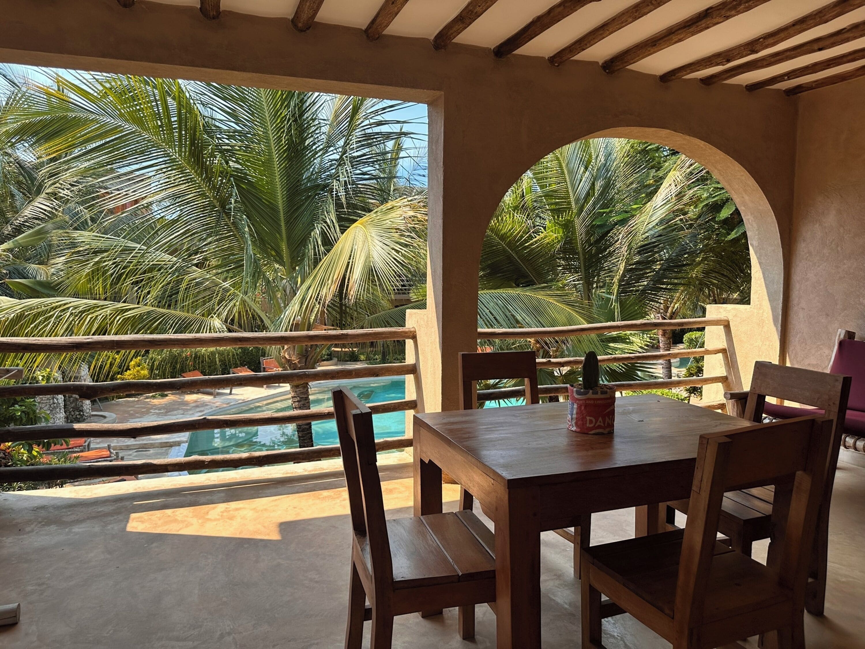 Una mesa y sillas de madera en un balcón con vista a una piscina y palmeras.