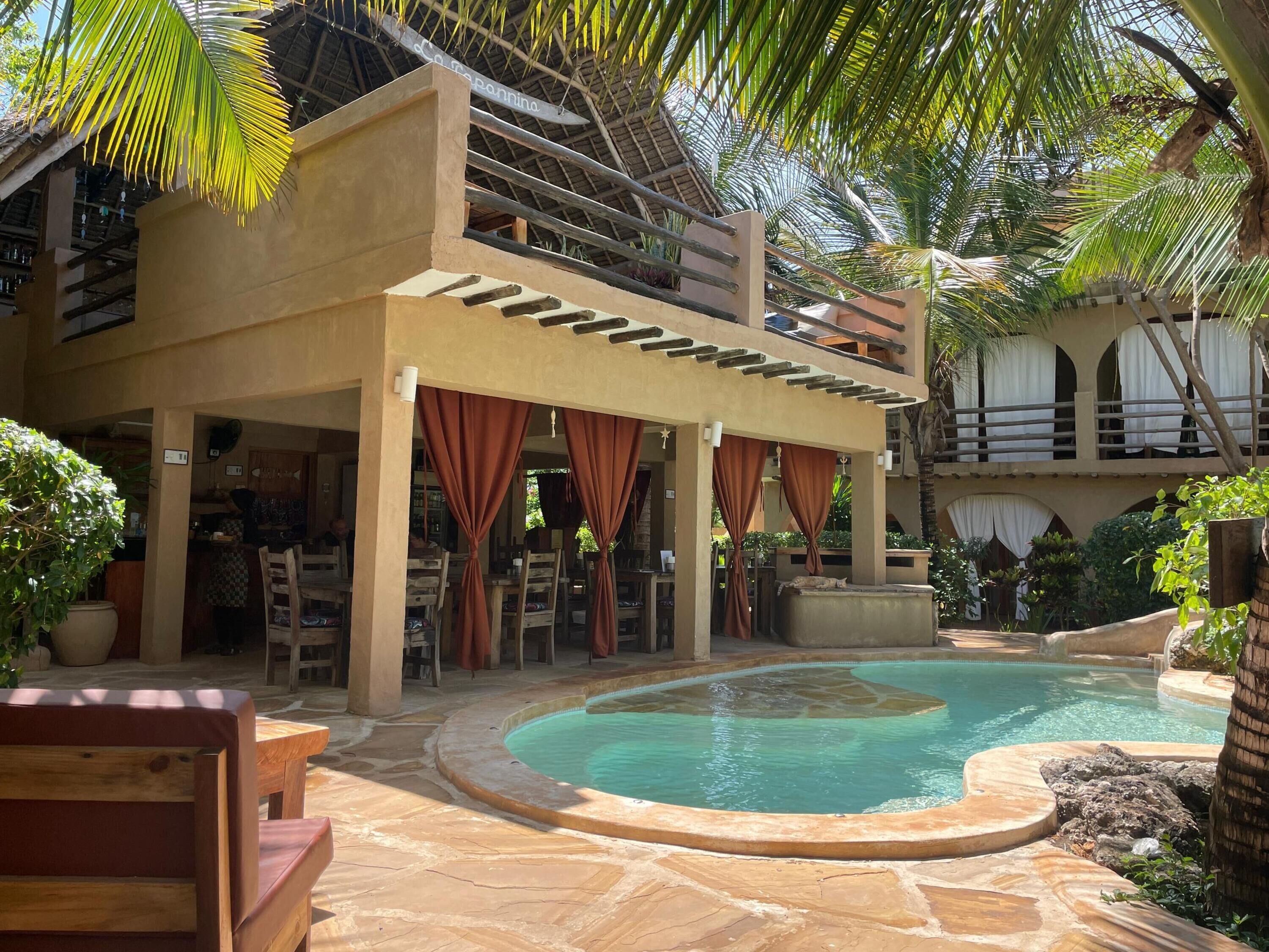 A pool area with a curved pool, outdoor seating, and a covered patio with curtains.