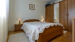 A bedroom with a wooden bed, a nightstand with a lamp, a wardrobe, and a framed picture on the wall. - Apartment Petar (Konavle)