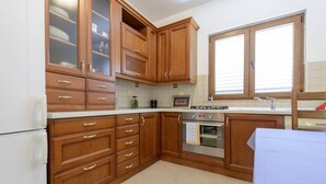 A kitchen with wooden cabinets, a stainless steel oven, and a window with blinds. - Apartment Petar (Konavle)